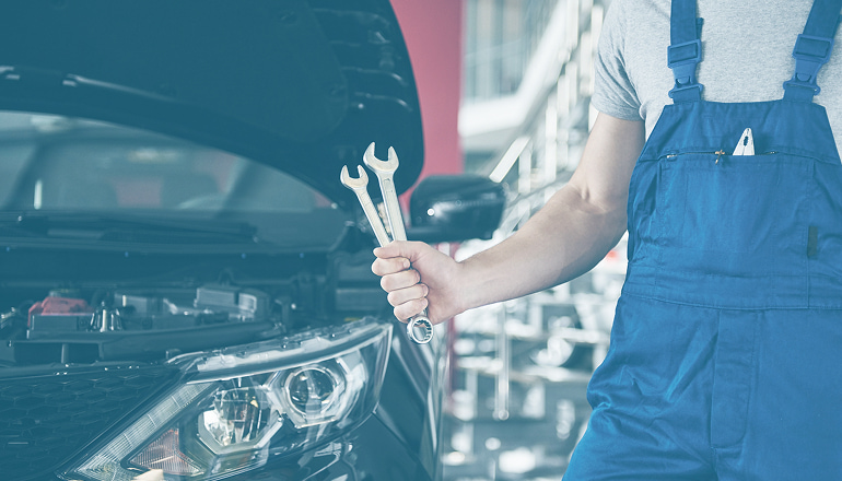mecanico con herramientas en la mano y un coche detrás sin saber cumpliendo con los plazos del seguro para reparar un siniestro